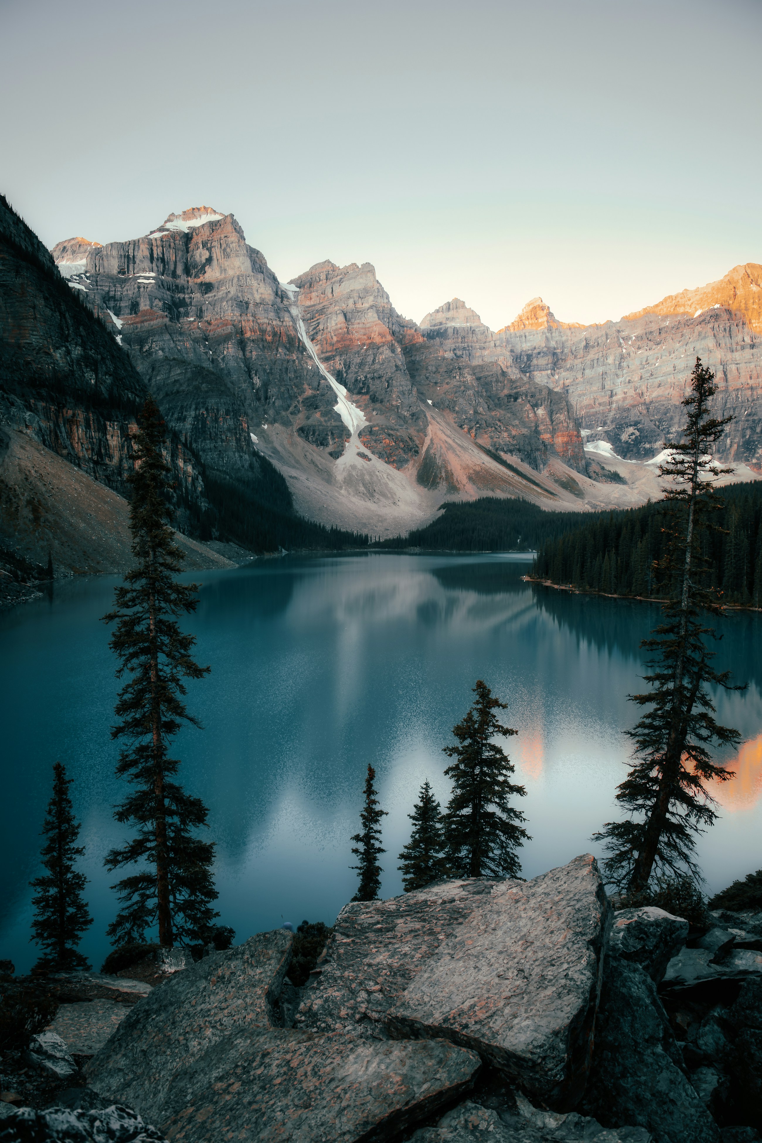 Warm sunlight touching mountain peaks above the cool blue water of Moraine Lake